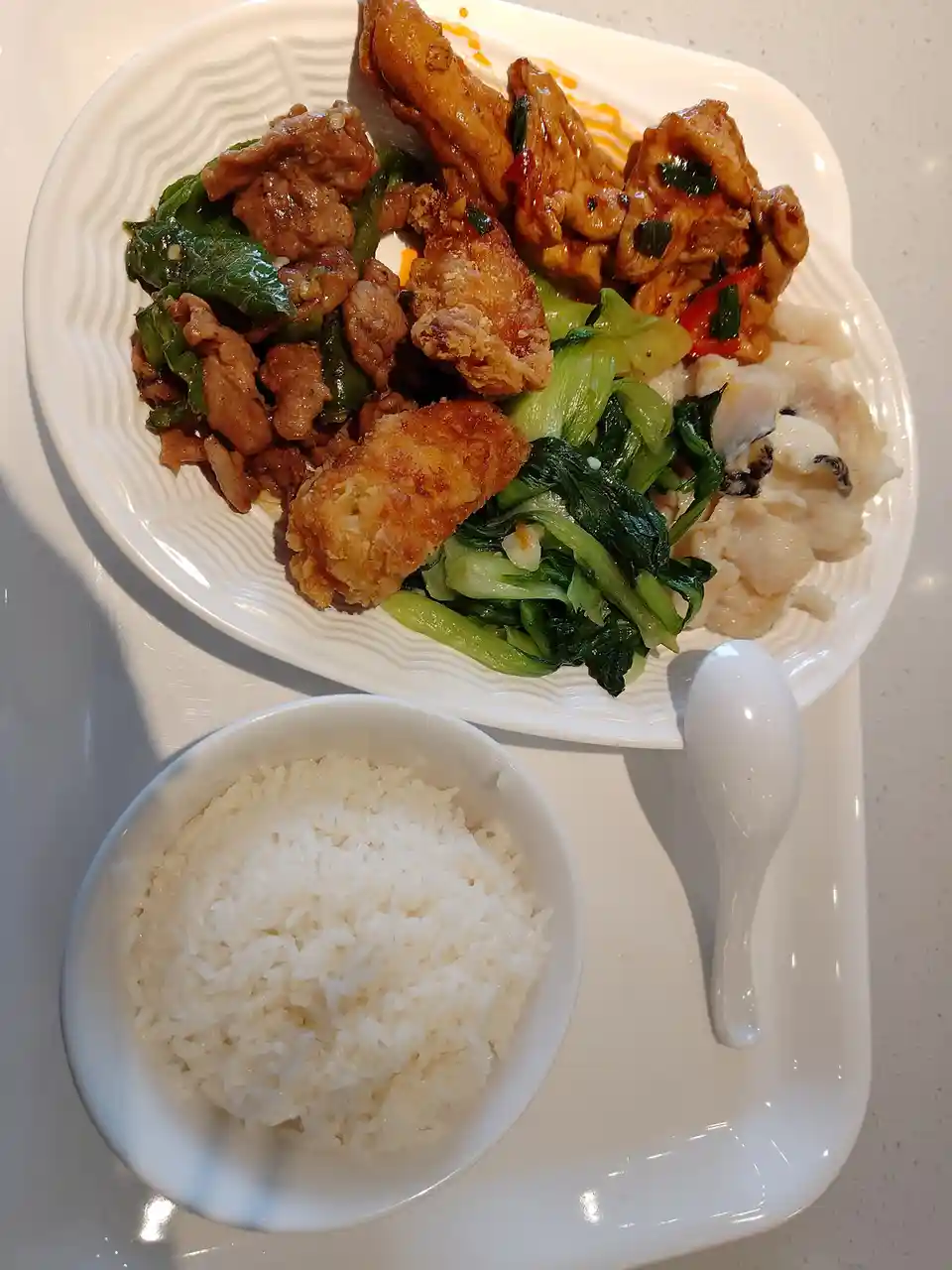 A white tray holds a large plate of assorted Chinese dishes including stir-fried meat with green peppers, fried chicken…