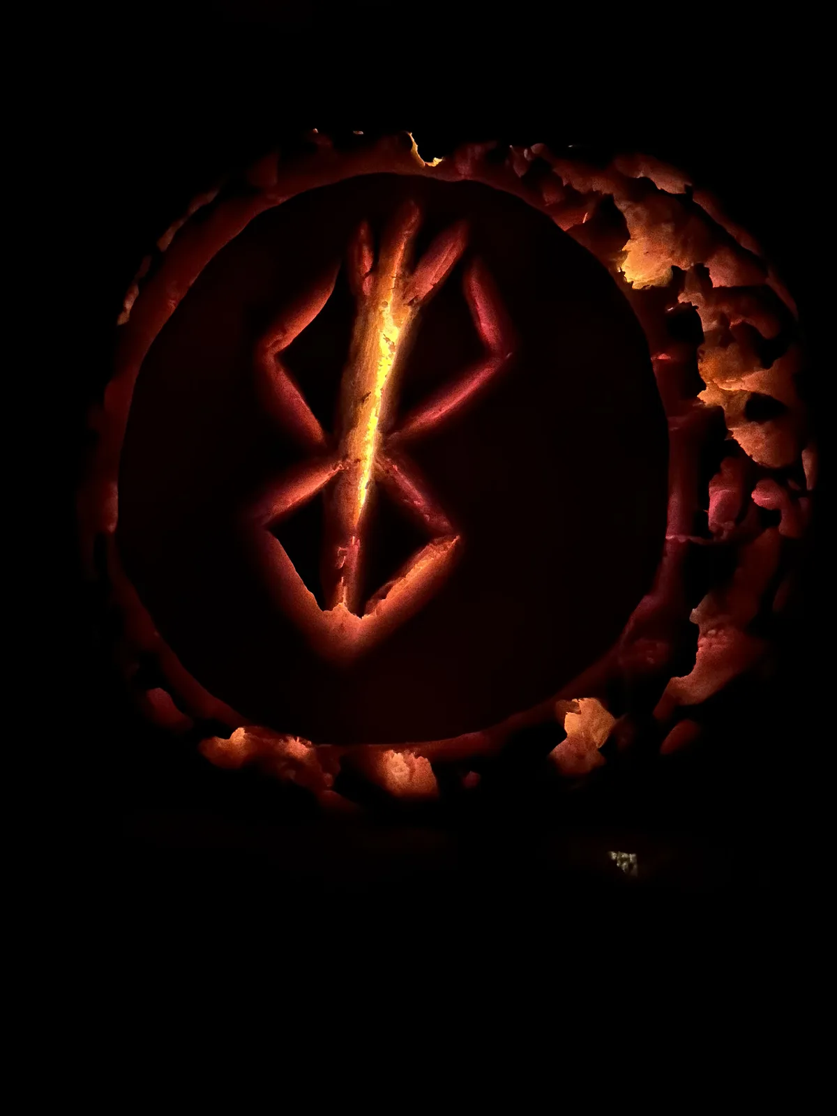 A carved pumpkin with a glowing orange interior displays the Bluetooth logo, a stylized 'B' with two curved lines…