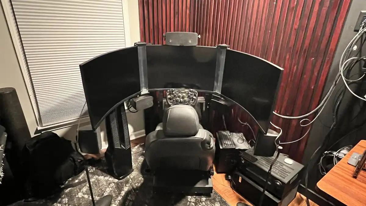 A room features a high-end flight simulator setup with a racing-style cockpit seat, a detailed steering wheel controller…