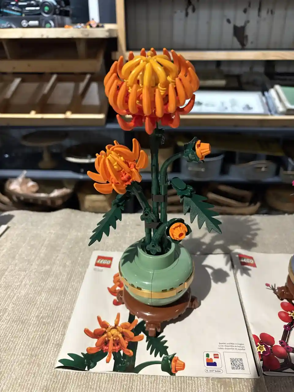 A completed LEGO set (set number 10368) depicting a detailed orange and yellow chrysanthemum flower with green leaves and…