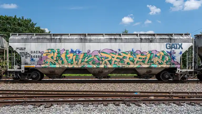 A silver GATX freight train car covered in colorful graffiti, including the word 'STRAIGHT' in large letters, sits on…