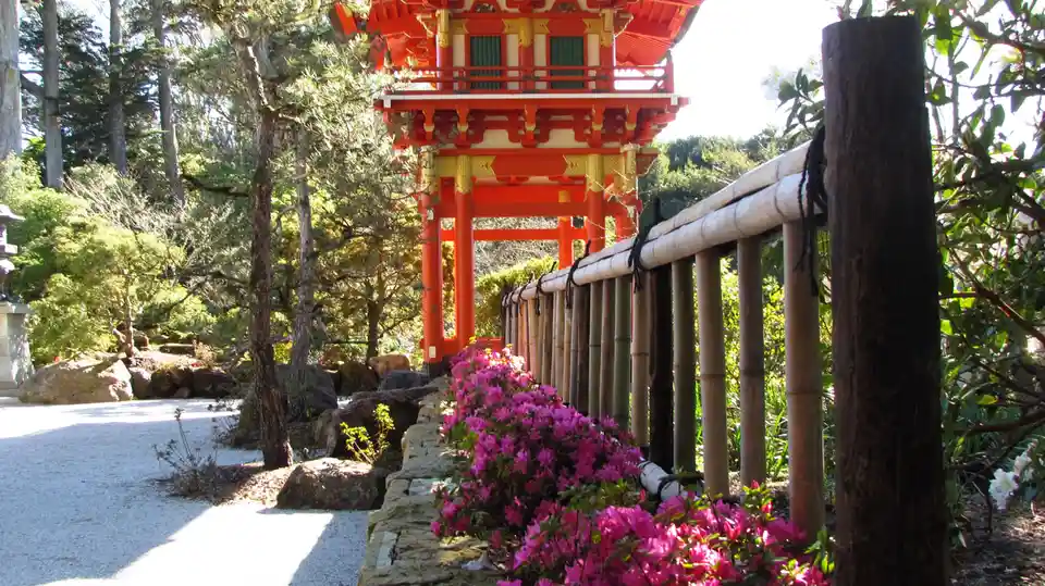A serene Japanese garden scene featuring a bright red and gold traditional pagoda structure in the distance, framed by lush…