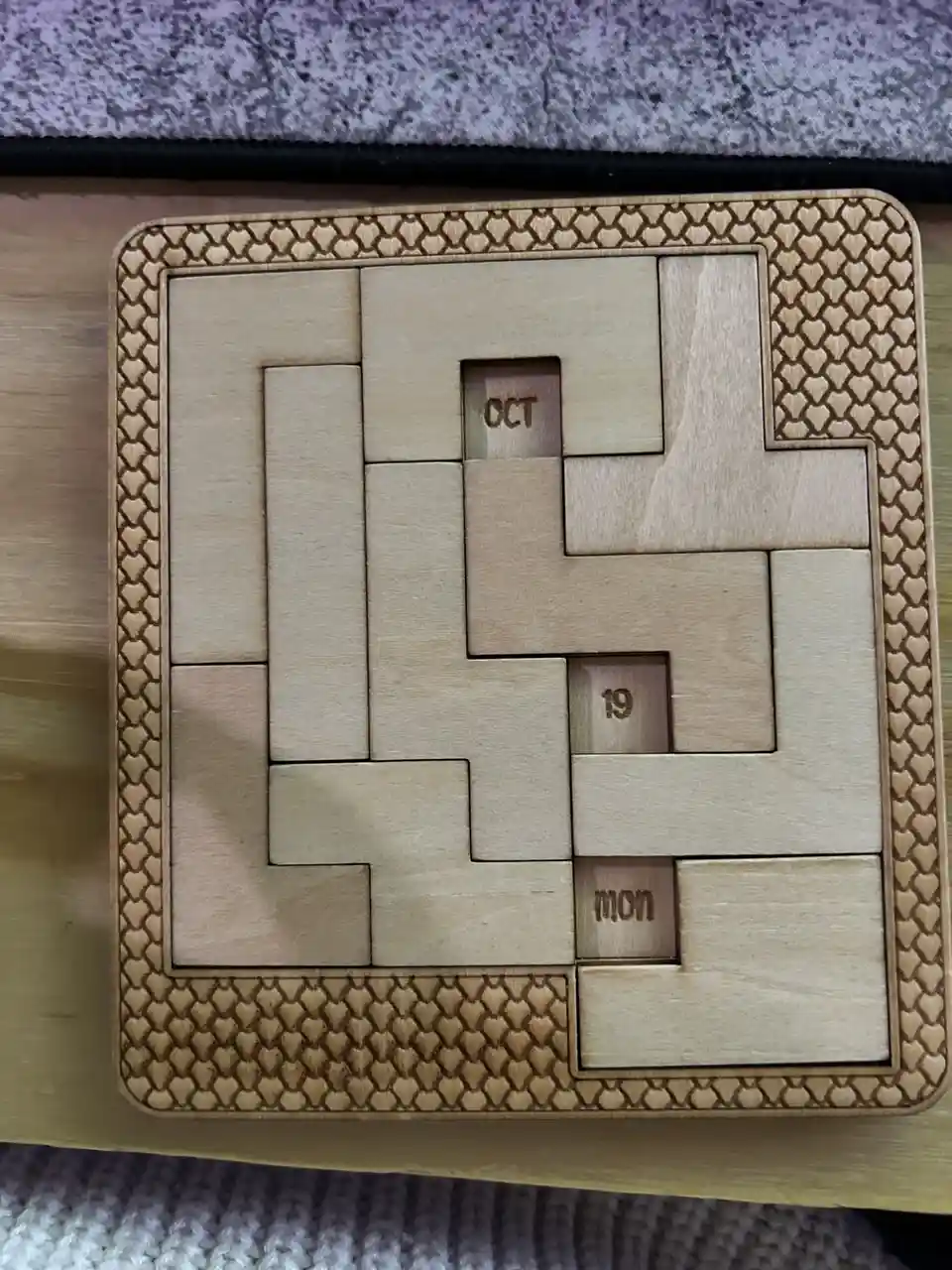 A wooden puzzle calendar with interlocking pieces, three of which are labeled 'OCT', '19', and 'MON', forming the date…