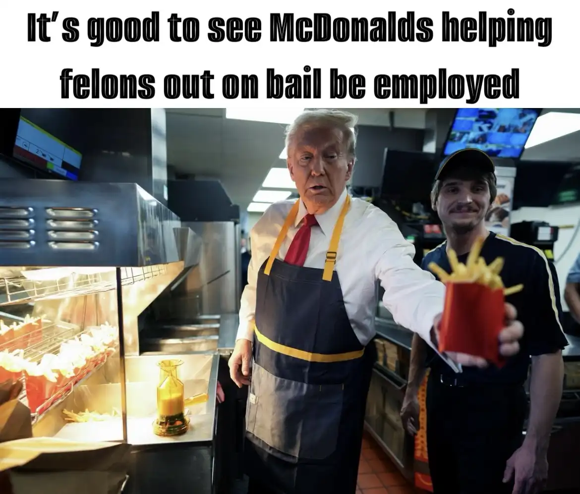 A man resembling Donald Trump in a McDonald's uniform holds out a container of fries, while another man in a uniform stands…