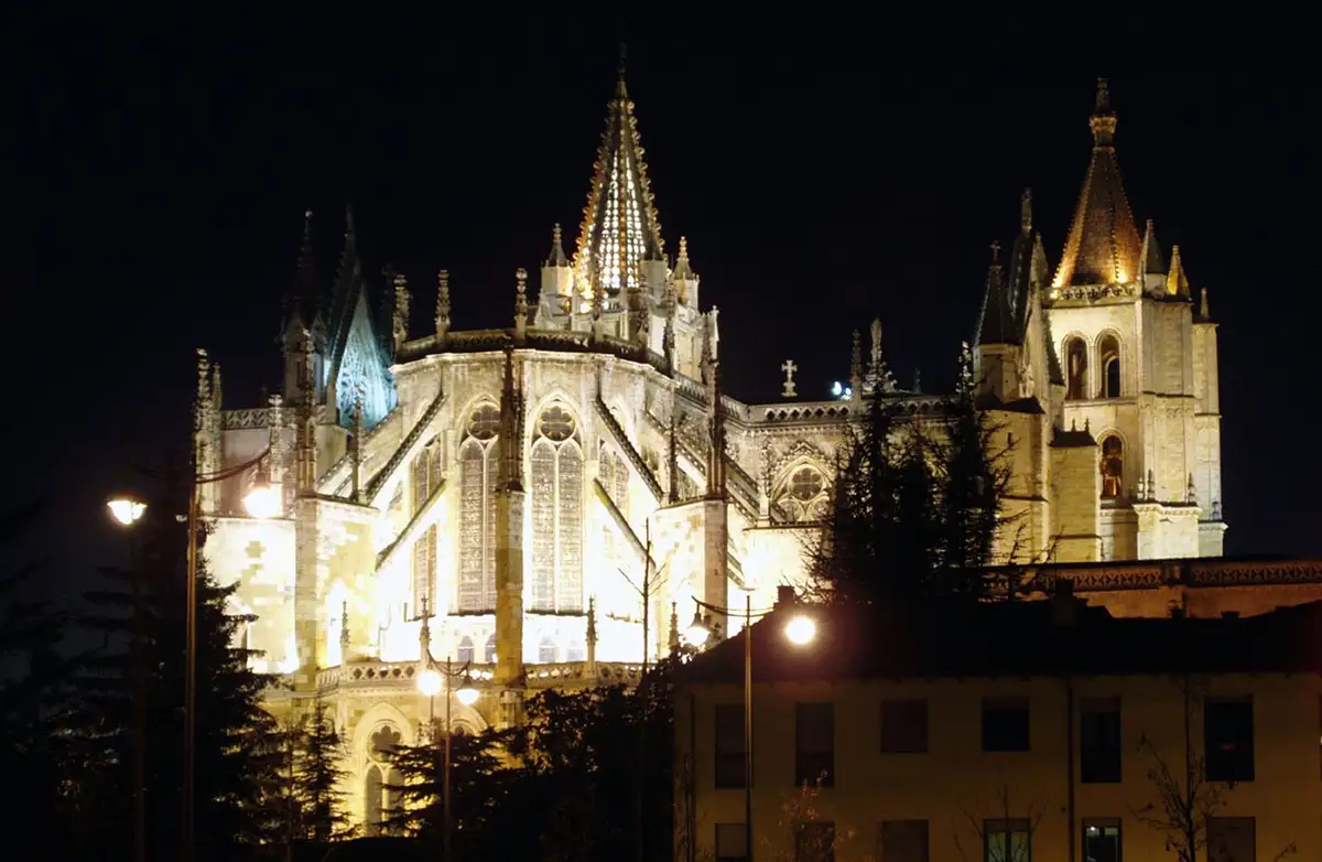 A nighttime photograph of a grand, illuminated gothic cathedral with multiple spires and ornate windows, set against a dark…