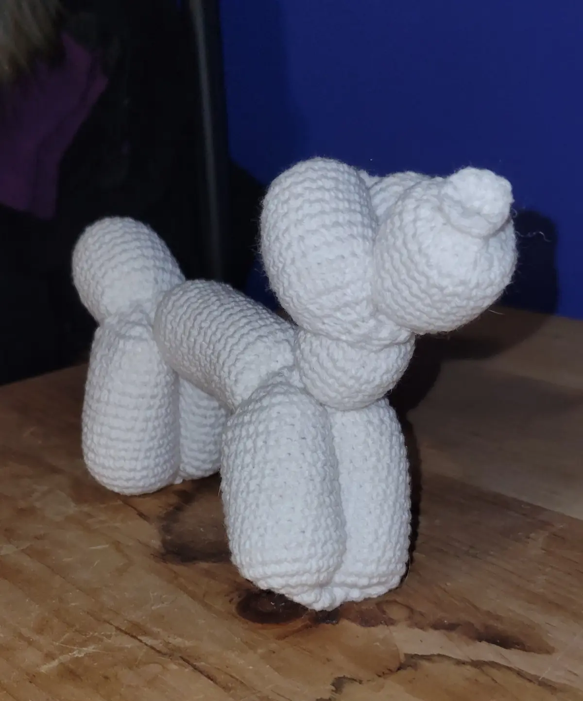 A white crocheted dog toy, styled to resemble a balloon animal with rounded segments for legs, body, and head, sits on a…