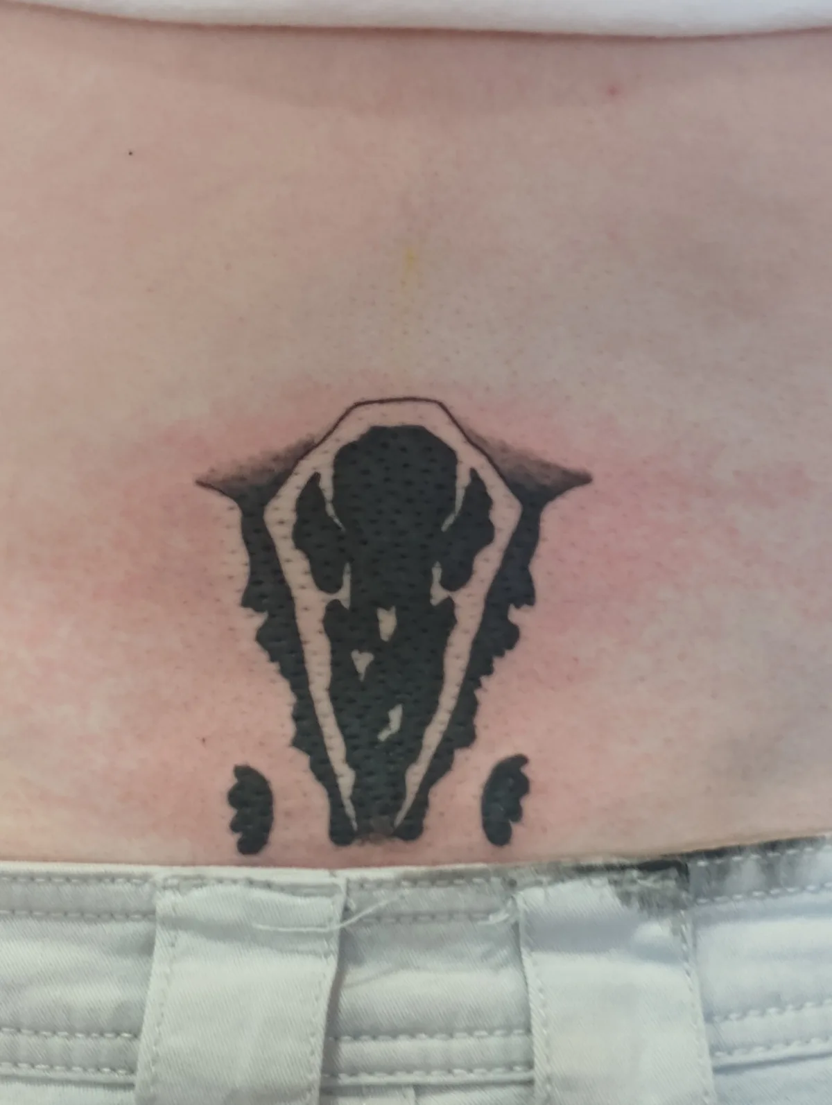 A close-up photo shows a fresh black-and-white tattoo on a person's lower back, just above light-colored denim pants. The…