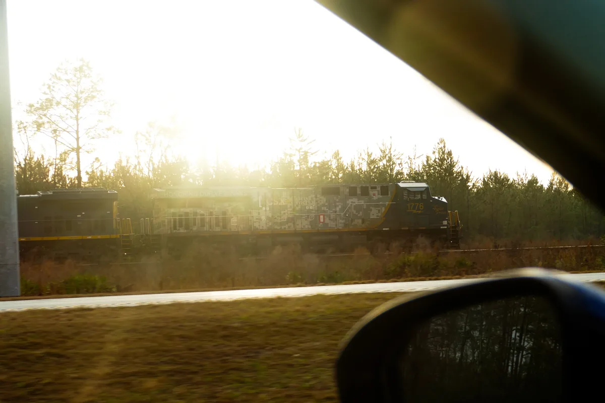 A photograph taken from inside a moving car shows a CSX train with a camouflage livery and the text 'HONORING OUR VETERANS'…