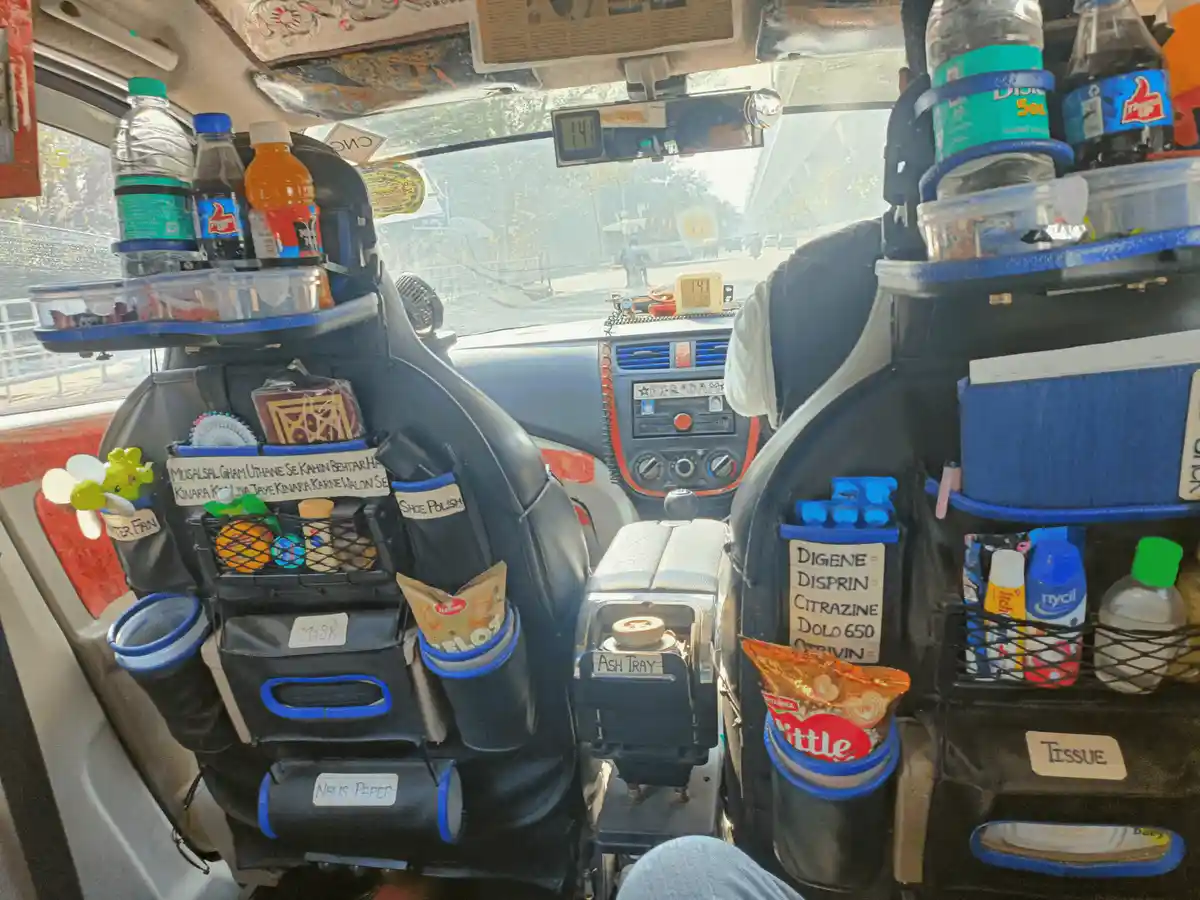 The interior of a heavily customized auto-rickshaw shows both front seats covered in black organizers with blue trim…