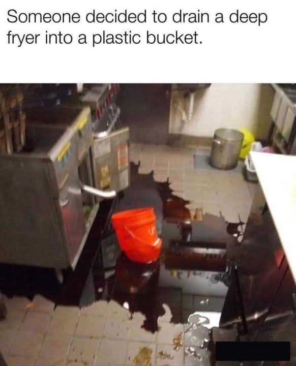 A kitchen scene shows a large, dark puddle of oil spreading across tiled flooring, originating from a deep fryer. An orange…