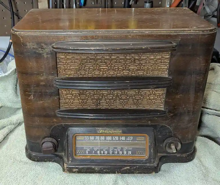 A close-up of a vintage, weathered brown Westinghouse tube radio with a woven speaker grille and a detailed dial showing…