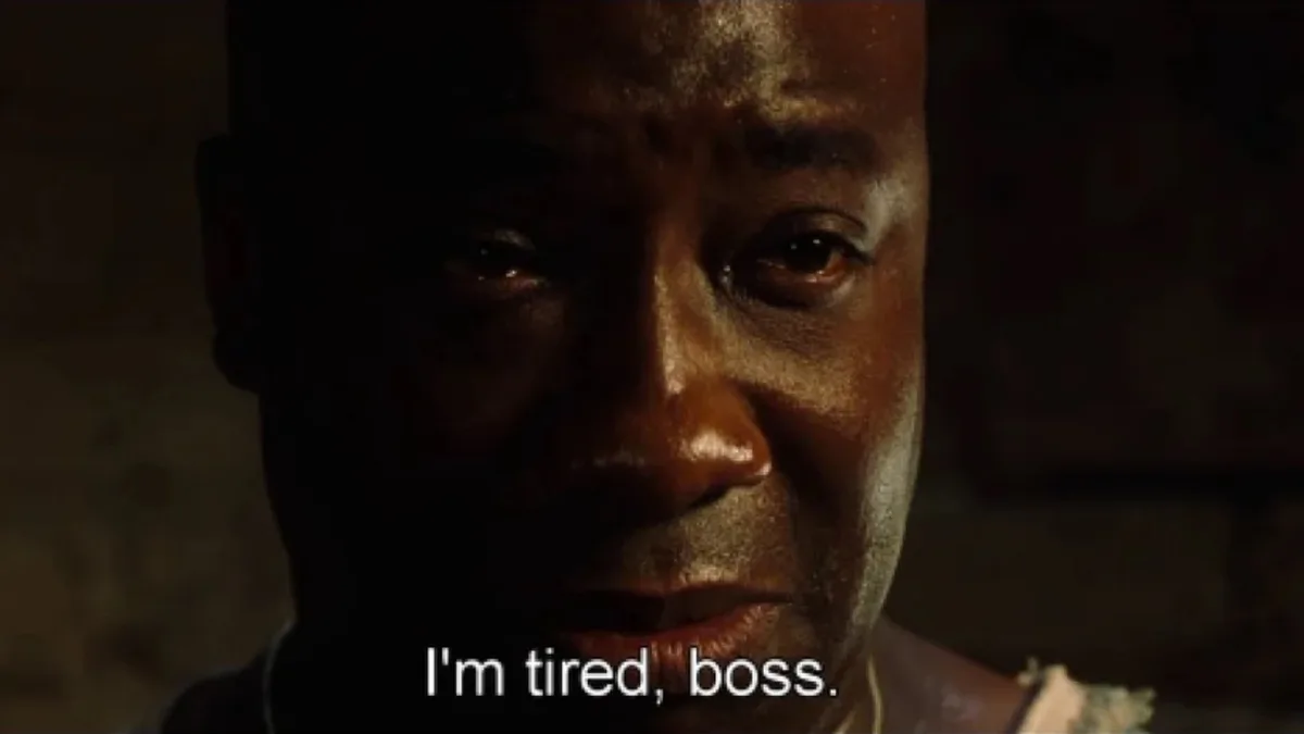 A close-up shot of a man with a weary, exhausted expression, his face illuminated by dim, warm lighting against a dark…