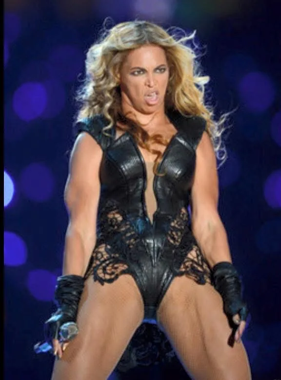 A woman with long blonde hair wearing a black leather and lace bodysuit and gloves, holding a microphone, makes a fierce…