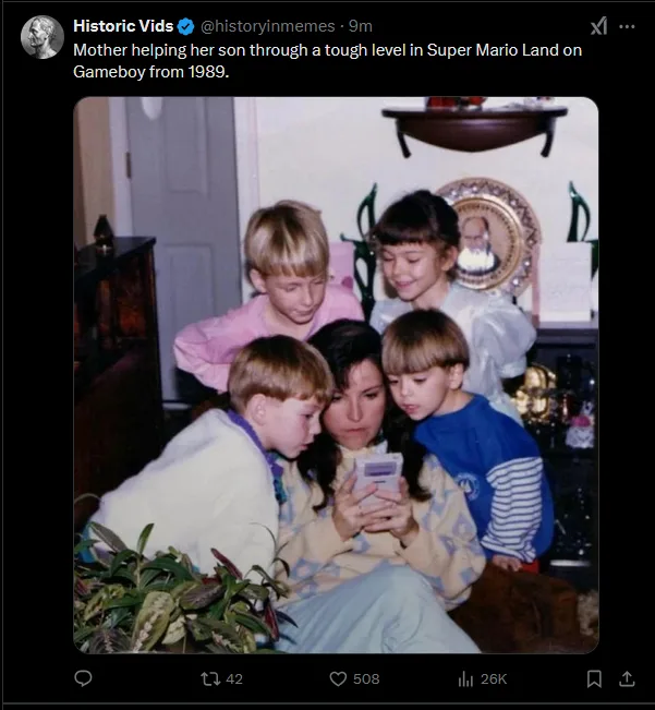 A vintage 1989 photo shows a woman sitting on a couch surrounded by three young children, all intently focused on a handheld…