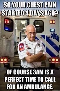 A bald, bespectacled paramedic in a white uniform with a red cross patch stands with arms crossed in front of an ambulance…