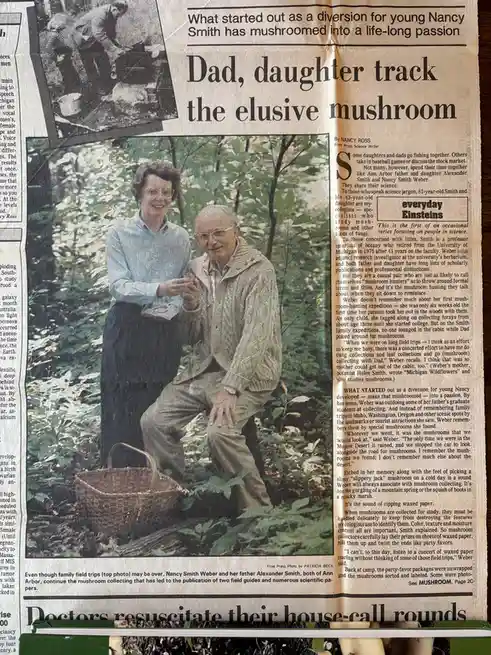 A newspaper clipping shows an older man and woman in a forest, smiling while holding a mushroom, with a basket nearby. The…