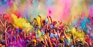 A vibrant, crowded scene of people celebrating Holi, throwing colorful powders into the air, with arms raised in joy…