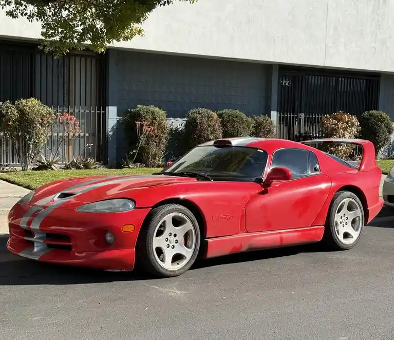 a red dodge viper gts sports car with silver racing stripes is parked on a street in front of a building with bushes and a…