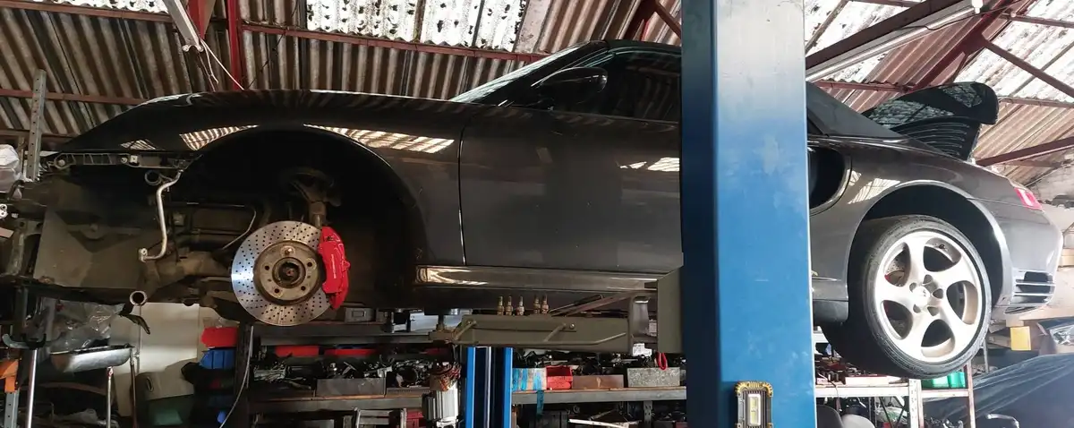 A black Porsche 911 is elevated on a car lift in a garage, with its front wheel removed and the rear wheel still on the…