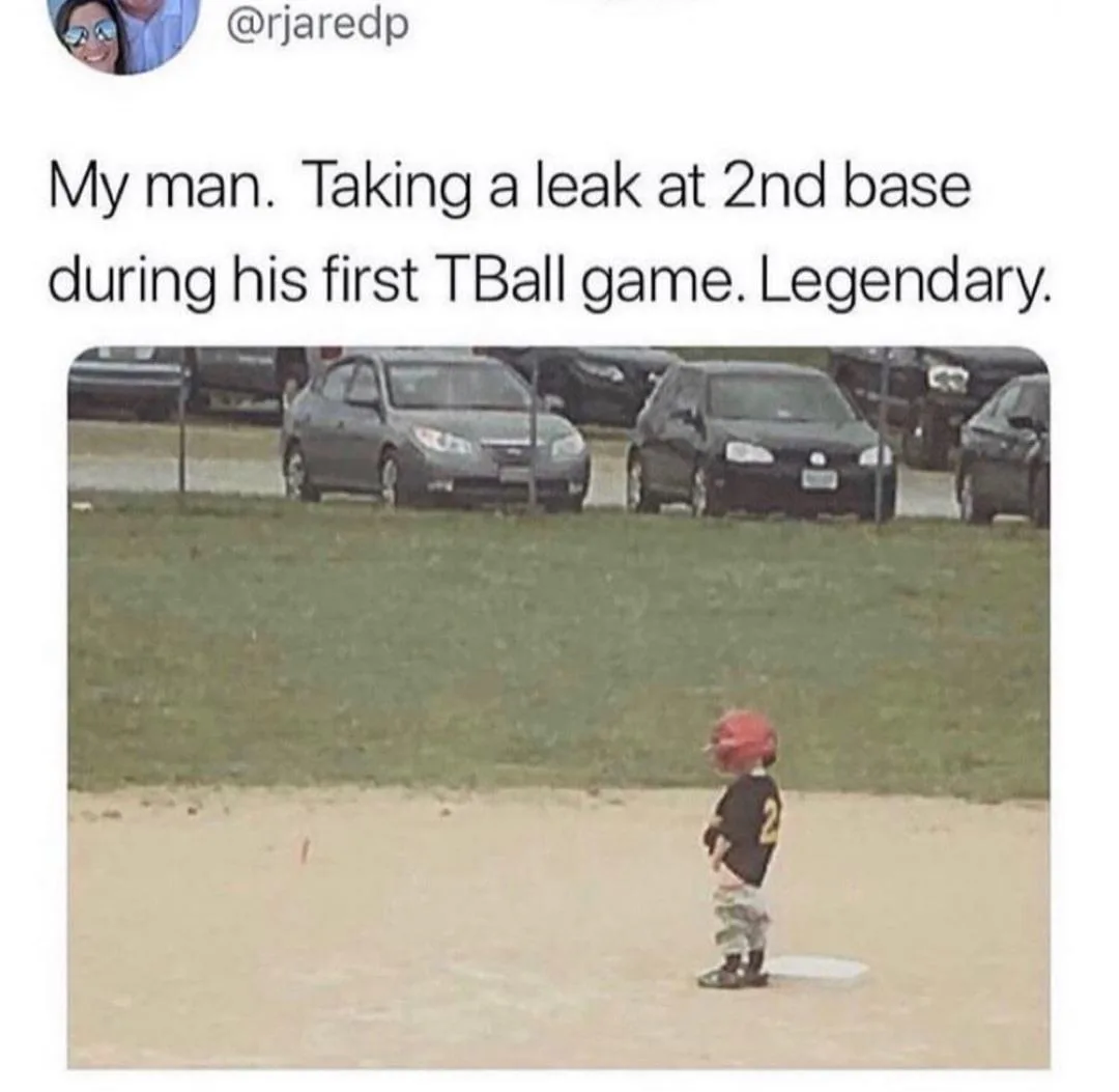A young child wearing a red baseball helmet and a black jersey with the number 2 stands on a baseball field, positioned on a…