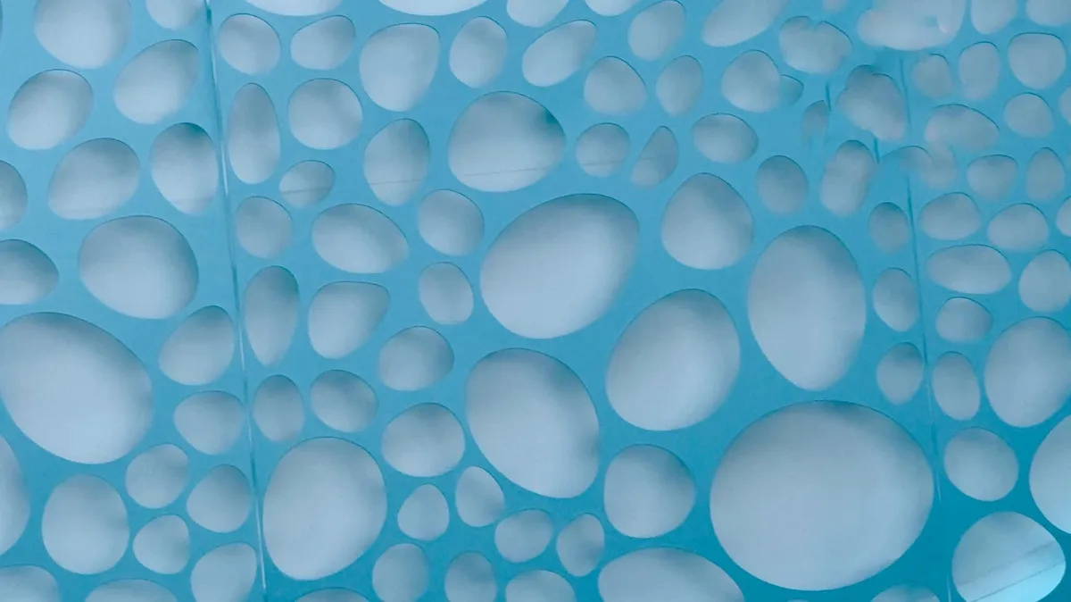 The image shows a close-up of a blue, textured surface with numerous irregularly shaped oval cutouts, resembling a…