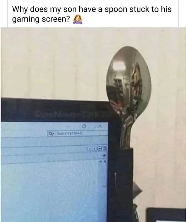 A shiny metal spoon is visibly stuck to the top right corner of a computer monitor displaying a search interface. The…