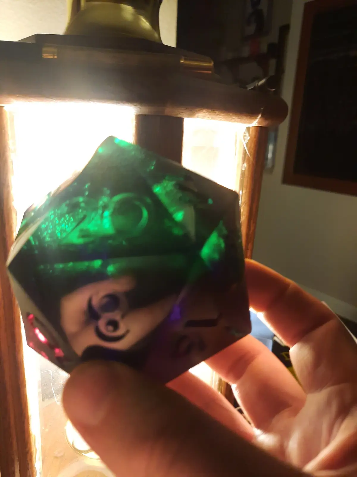 A hand holds a translucent green twenty-sided die (d20) with the number 20 visible on one face, illuminated by a bright…