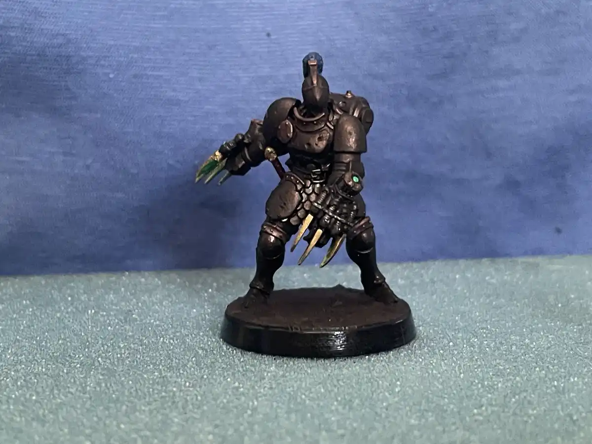 A painted miniature of a heavily armored, helmeted warrior with green-tipped claws on one hand and golden spikes on the…
