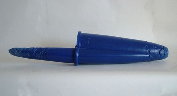 A blue plastic knife with a blue plastic handle is shown lying on a white surface. The blade is covered in a blue plastic…