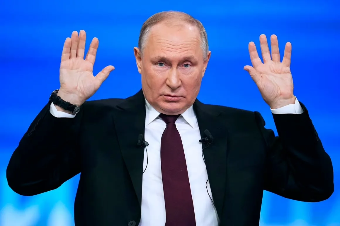 a man in a black suit and maroon tie stands against a blue background, raising both hands palms outward with a stern…