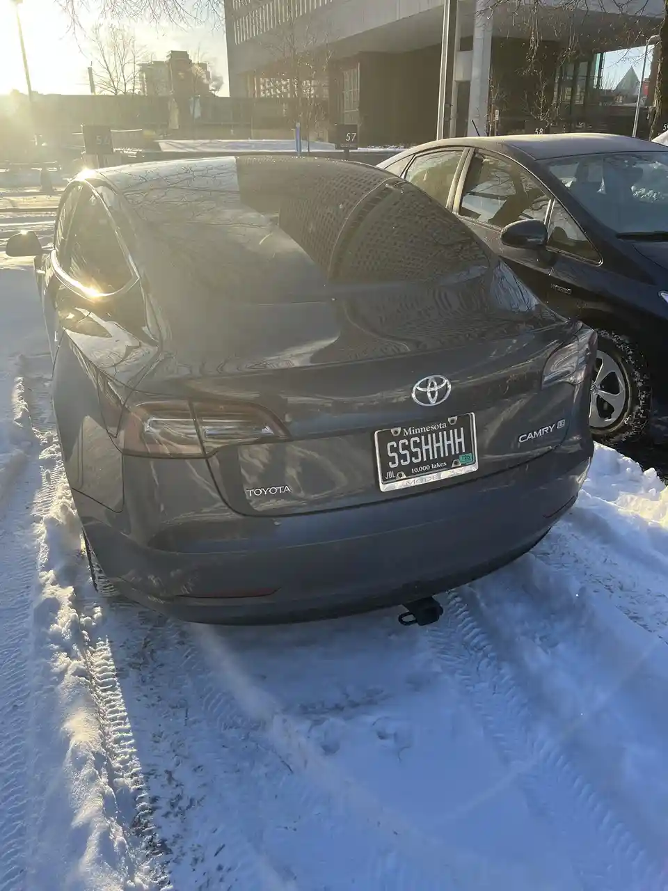 A dark gray Toyota Camry Hybrid is parked in snow with its rear facing the camera, showing a Minnesota license plate that…
