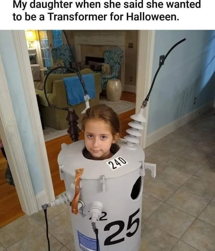A young girl with brown hair is wearing a homemade Halloween costume made from a large white electrical transformer…