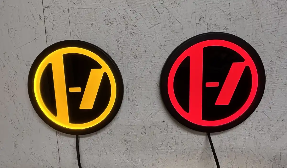 Two circular illuminated signs mounted on a textured wall, one glowing yellow and the other red, both displaying the…