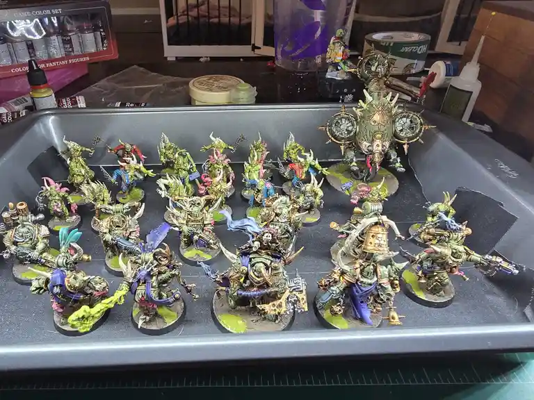 A tray filled with numerous intricately painted fantasy miniatures, mostly green-skinned orcs or goblins with varied weapons…