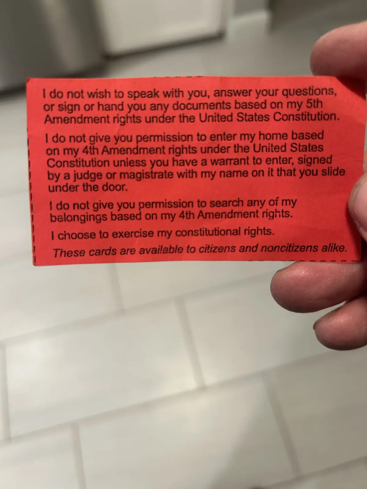 A hand holds a red card with black text listing constitutional rights against police questioning and home searches…