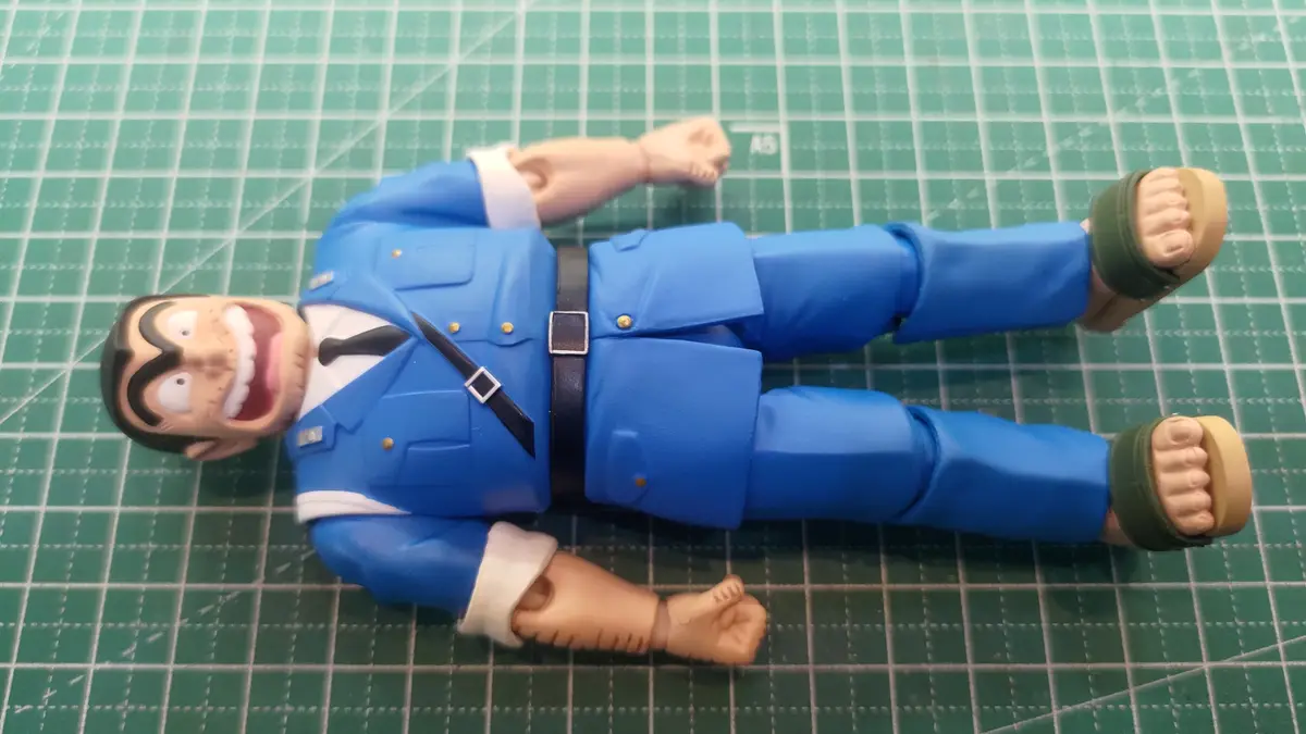 A plastic action figure of the anime character Inspector Gadget lies flat on its back on a green cutting mat, mouth wide…