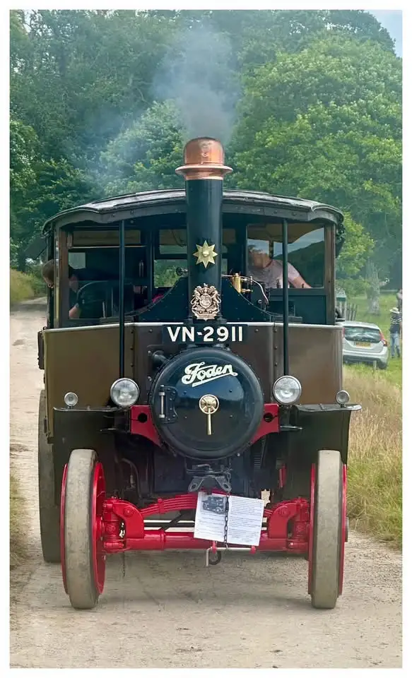 A vintage steam-powered Foden vehicle, marked with the registration VN-2911, emits smoke from its chimney while parked on a…