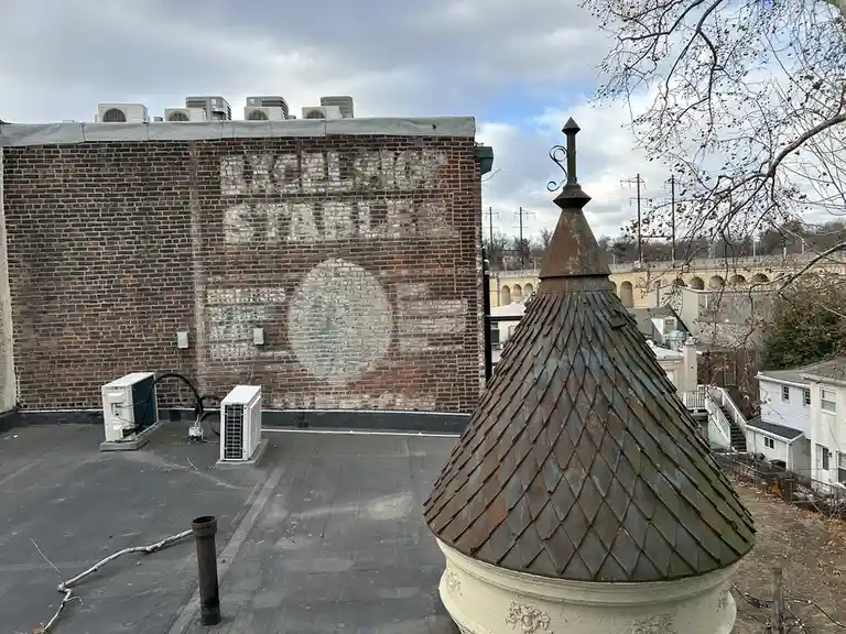 A rooftop view shows a weathered brick wall with faded white paint spelling 'FACILITIES STAFF' and a large circular logo. In…