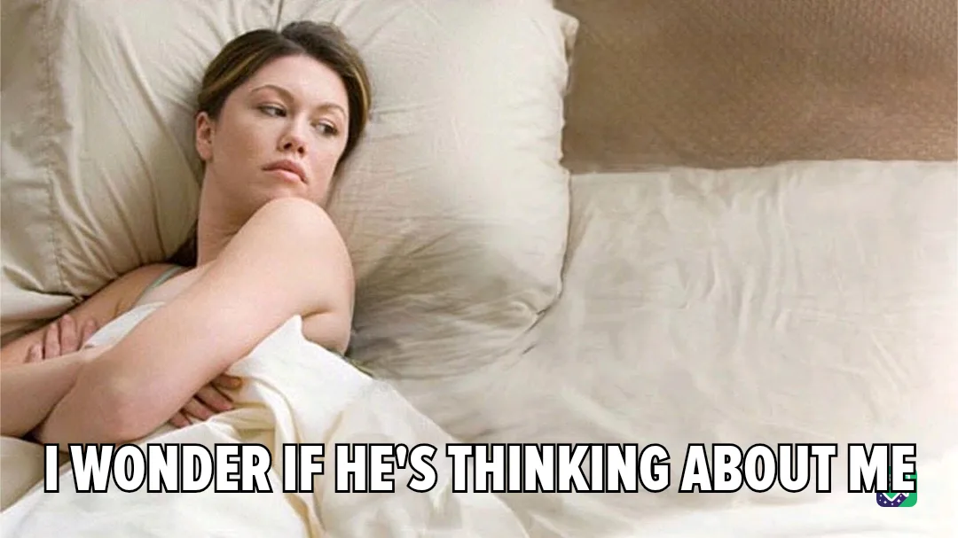 A woman lies in bed under white sheets, propped up on pillows, looking pensive and slightly sad. Her arms are crossed over…