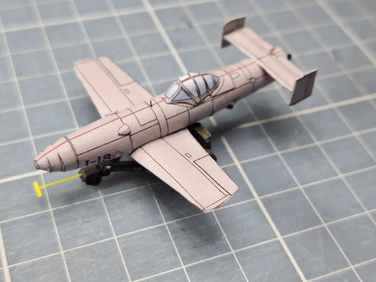 A small, light-colored paper airplane model with visible construction lines and a cockpit, resting on a gray grid-patterned…