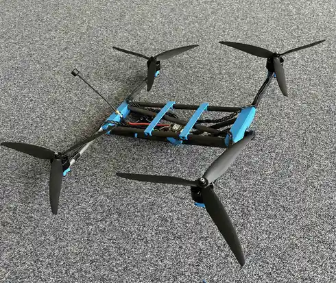 A custom-built quadcopter drone with a blue and black frame lies on a gray carpet, its four propellers visible and…