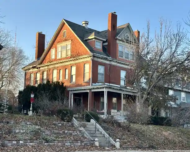 a large, two-story red brick house with multiple chimneys and a front porch, surrounded by bare trees and fallen leaves…
