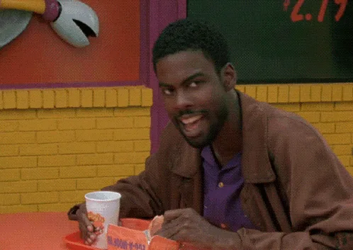 A man in a brown jacket and purple shirt sits at a fast-food counter, smiling at first, then his expression shifts to…