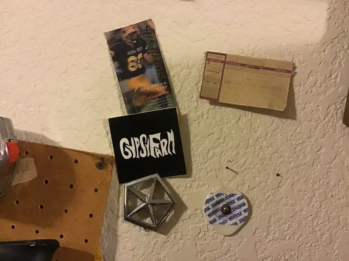 A close-up of a textured white wall with several items pinned to it: a New Mexico State Sun Devils football program from…
