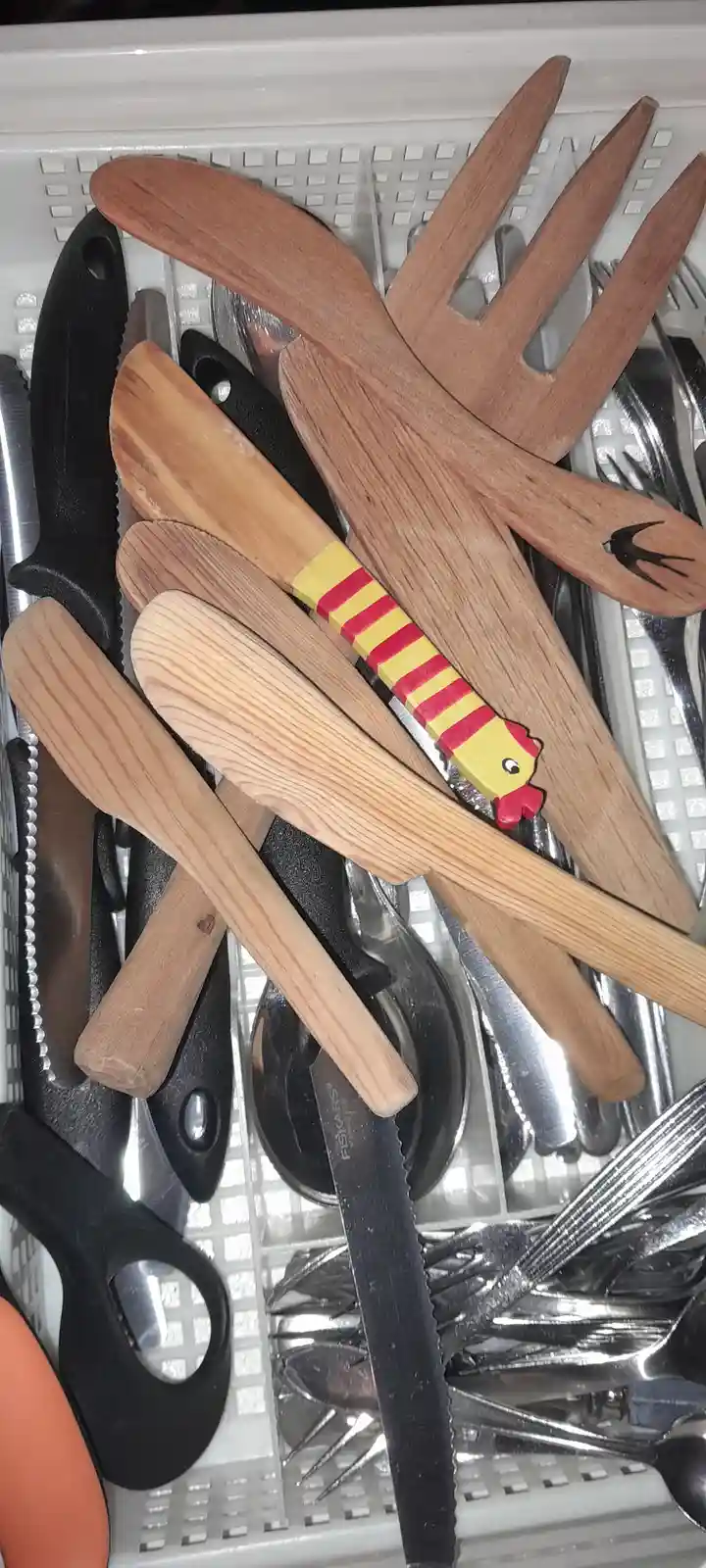 A close-up photo shows a cluttered kitchen drawer filled with various utensils, including wooden spoons, forks, and metal…
