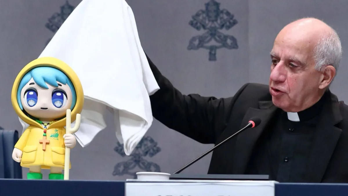 A man in a black clerical collar suit is at a podium, holding a white cloth over a yellow hooded anime-style figurine with…