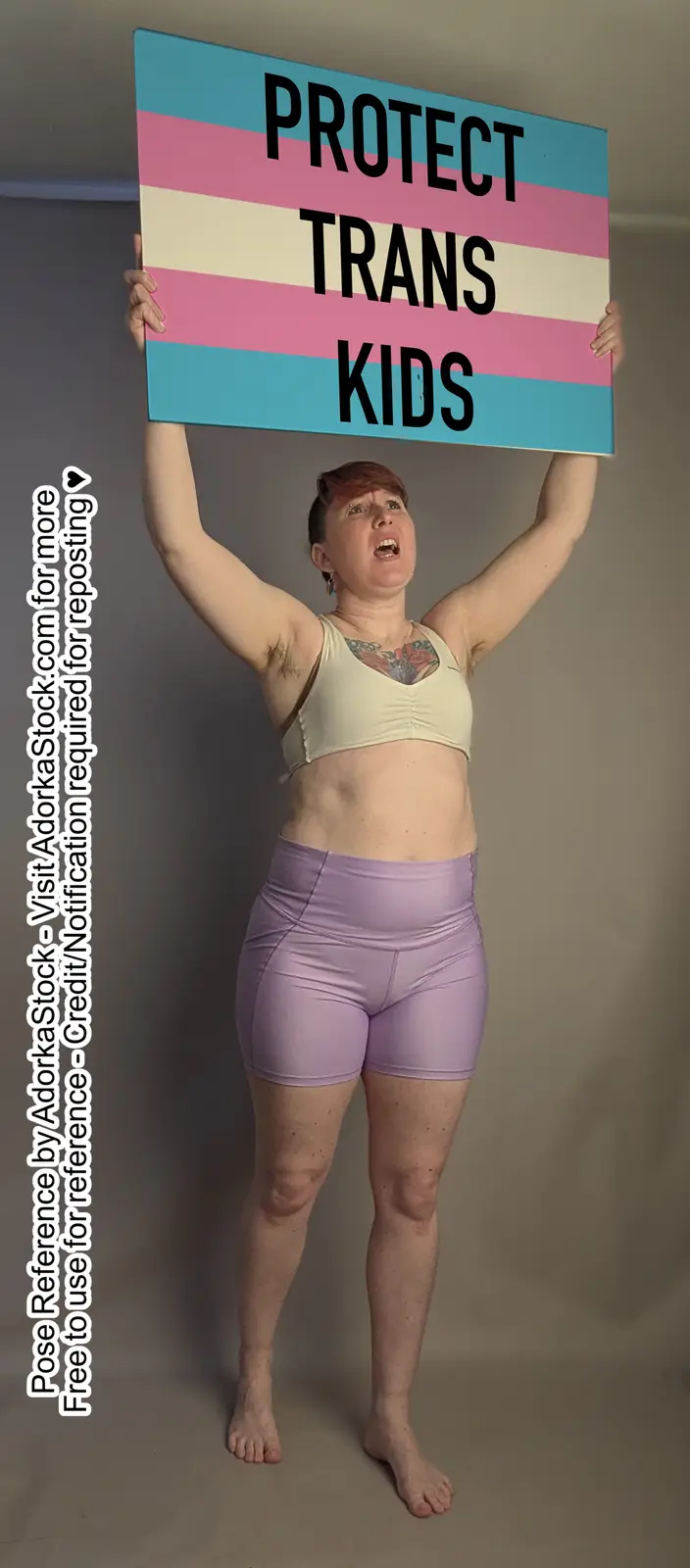 A person with short hair and visible chest hair holds up a sign with the trans flag colors and the text 'PROTECT TRANS…