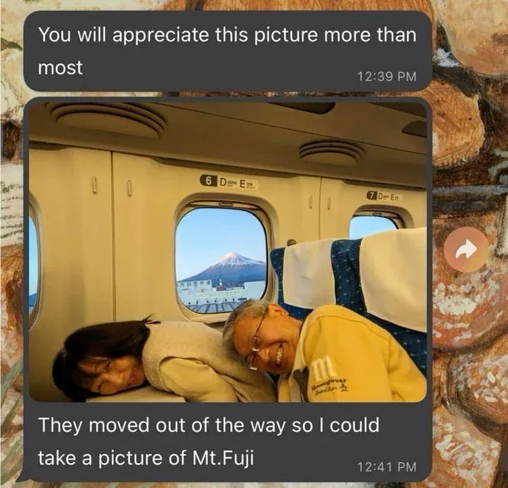 A screenshot of a text conversation shows a photo of two people sleeping on a train seat, with Mount Fuji visible through…