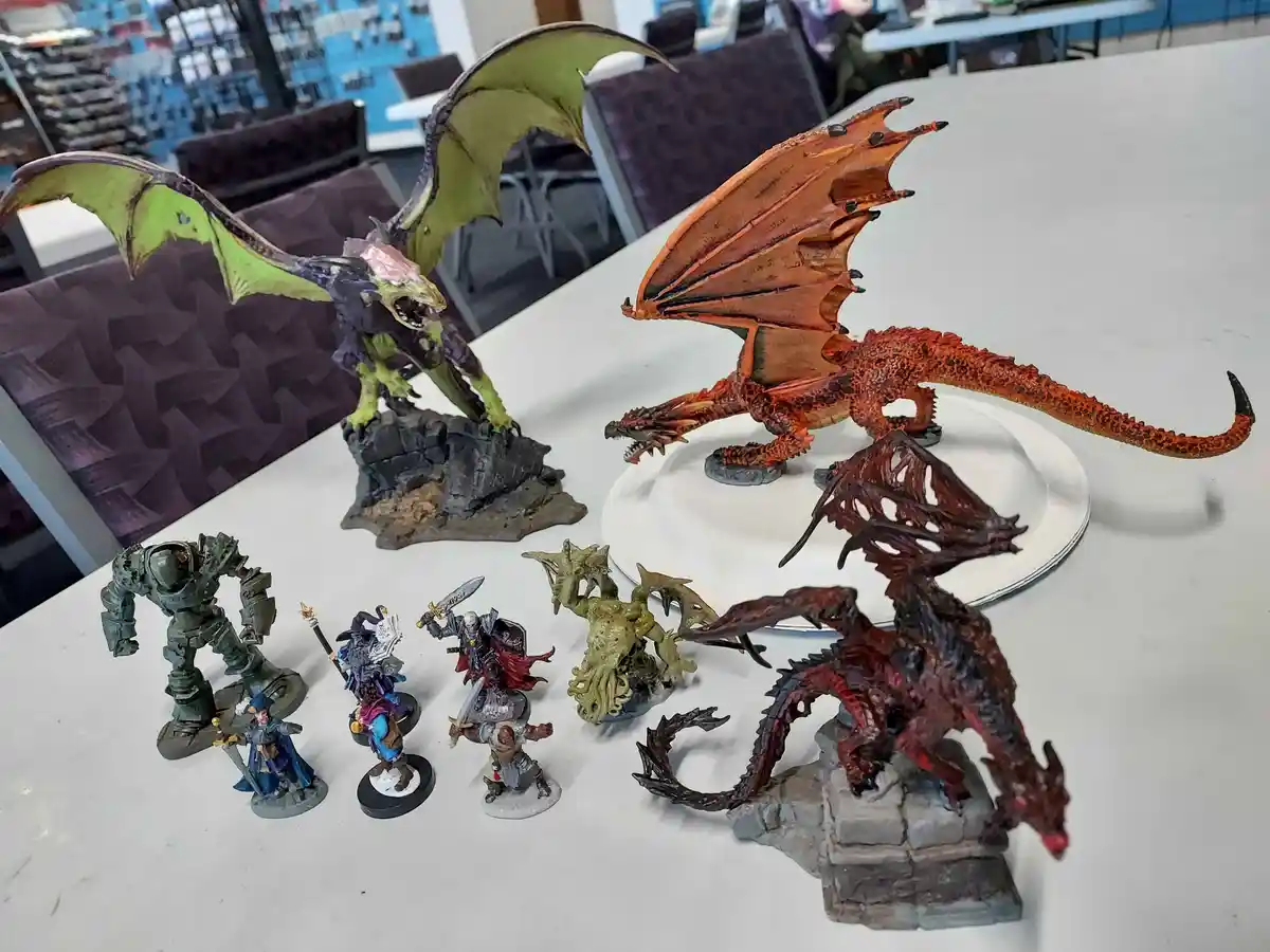 A collection of painted fantasy miniatures, including three large dragons (green, orange, and red) and several smaller…