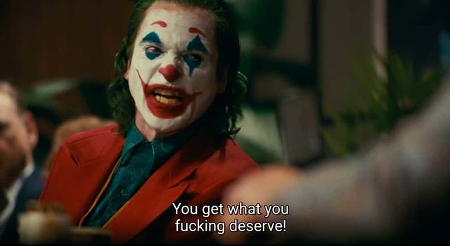 A close-up of the Joker from the movie 'Joker' (2019), wearing his iconic red suit and clown makeup, with a furious…